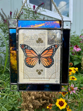 Load image into Gallery viewer, Orange monarch butterfly painted in Gouache on vintage floral encyclopedia, and pressed leaves set between glass with blue and gold mirrored glass border and clear beveled corners.  Rectangle shape with brass hanging chain at top. 
