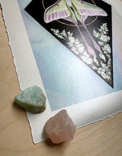 Load image into Gallery viewer, Photo showing bottom left angle of print. Print has slight shimmer to it in changing light. Full view - print on paper of Chinese moon moth and meadowsweet on black background, diamond shape. This sits in a white iridized glass background. There is a gold circle around the center of the moon moth. Meadowsweet flower painted below and surrounding moths lower wing tendrils.