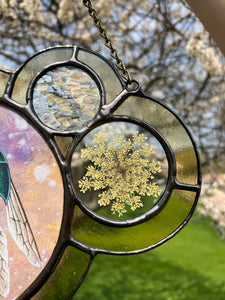 Close up of Wild carrot with smaller textured circle above - Jewel wasp (green and dark blue) on dyed light pink/yellow/purple paper as central piece in large left circle. Two more circles on right side. Second smallest encases pressed Wild carrot in clear glass. Smallest circle is above Wild carrot with textured iridescent glass. Entire piece has light yellow border.