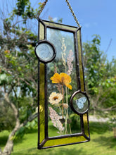Load image into Gallery viewer, Close up - Wildflowers and yellow poppy encased in glass with yellow glass borders segmented by two light blue moth circles. Rectangle shape with brass hanging chain at top. Center glass is clear.
