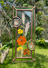 Load image into Gallery viewer, Wildflowers and orange cosmos  encased in glass with leaf green glass borders segmented by two bronze copper butterfly paintings encased in clear glass circles. Rectangle shape with brass hanging chain at top. Center glass is clear.
