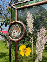 Load image into Gallery viewer, Close up - Wildflowers and orange cosmos  encased in glass with leaf green glass borders segmented by two bronze copper butterfly paintings encased in clear glass circles. Rectangle shape with brass hanging chain at top. Center glass is clear.
