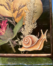 Load image into Gallery viewer, Close up of painted snail- Painted snail in gouache on paper with ressed rose petals, bee balm, and wild grasses with dark purple glass backing and glass end on bottom to mimic SNAIL SLIME. Rectangle shape with gold hanging chain.
