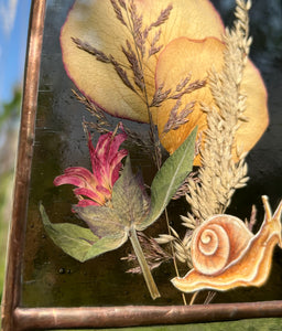 Close up of bee balm (pink) - Painted snail in gouache on paper with ressed rose petals, bee balm, and wild grasses with dark purple glass backing and glass end on bottom to mimic SNAIL SLIME. Rectangle shape with gold hanging chain.
