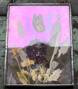 Image shows both iridescence and pink glass in low light. Painted monarch butterfly in gouache on paper with pressed butterfly bush flower, aster, and wild grasses with iridescent wispy pink glass backing. Rectangle shape with twine hanging.