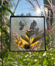 Load image into Gallery viewer, Alternate view with sun as backdrop. Honeybee painted in gouache on paper with wildflower grasses and  yellow sunflower and butterfly bush with clear textured glass backing. Square shape with gold chain hanger.
