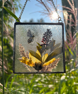 Alternate view with sun as backdrop. Honeybee painted in gouache on paper with wildflower grasses and  yellow sunflower and butterfly bush with clear textured glass backing. Square shape with gold chain hanger.