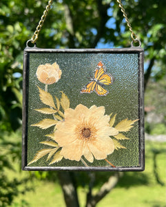 Alternate view with more light sun on piece. Monarch butterfly painted in gouache on paper with pressed Japanese anemone with textured clear glass backing Square shaped artwork with gold hanging chain.