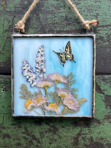 Swallowtail butterfly painted in gouache on paper with light pink aster, lavender, and silver lace fern with light wispy blue glass backing. Square shaped artwork with twine hanging.