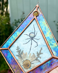 Spider with miniature landscape in body above pressed daisy flower and fern painted with gouache on paper set between glass. Iridescent floral textured glass border and yellow gem.