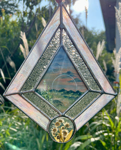 Gouache landscape set between glass with pressed wildflowers. Iridescent pink and textured clear glass border.