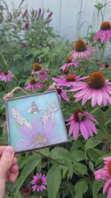 Load and play video in Gallery viewer, Video of artwork that begins with piece and moves to show real honeybee pollinating a purple coneflower - Alternate view - Honeybee painted in gouache on paper with wildflower grasses and  purple/pink cosmos flower with blue/green glass backing. Square shape with twine hanging.

