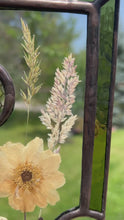 Load and play video in Gallery viewer, Video - Wild grasses and Japanese anemone encased in glass with dark green glass borders segmented by one gouache honeybee painting and one golden vinyl honeycomb pattern encased in clear glass circles. Rectangle shape with brass hanging chain at top. Center glass is clear.
