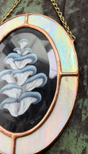 Load image into Gallery viewer, Right side view lose up to show rainbow iridized flash. Blue oyster mushroom gouache painting on black. Oval shaped glass hanging wall art with oval rainbow iridized glass border and chain
