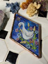Load image into Gallery viewer, Alternate view - low lighting - White goose painting on blue dyed paper with pink, blue, and yellow flowers surrounding it at the base. Gold painted sun above goose. Diamond shape. Gouache painting on hand dyed paper in beveled glass.
