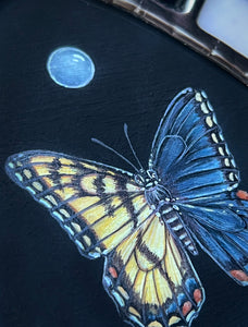 Close up of  bilateral gynandromorph swallowtail painting, above swallowtail there is a painted pearl circle.