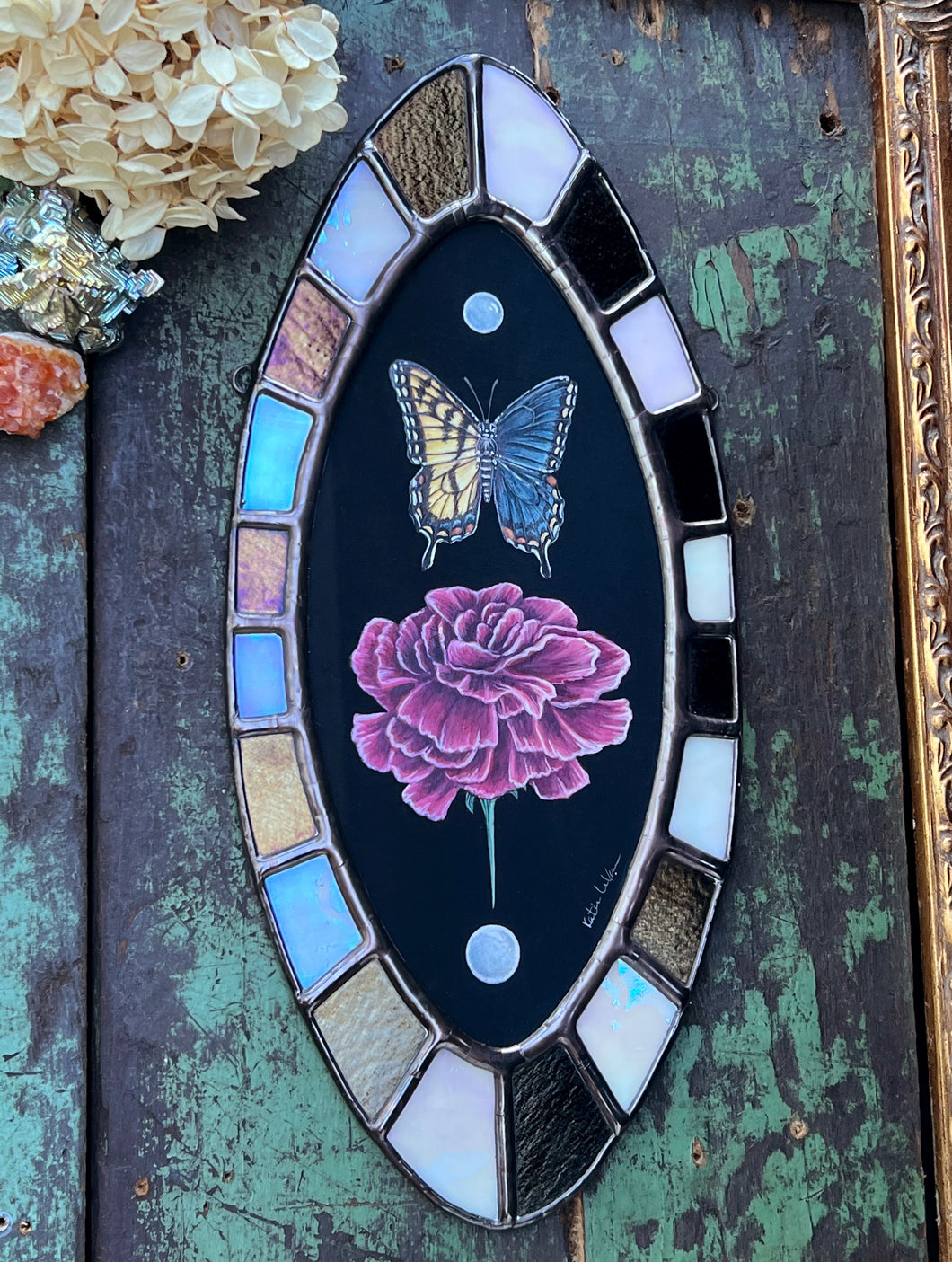 Full photo- bilateral gynandromorph swallowtail with pink carnations gouache painting, black background, encased in glass with bronze/black and white/opal checkered border. Oval shape.
